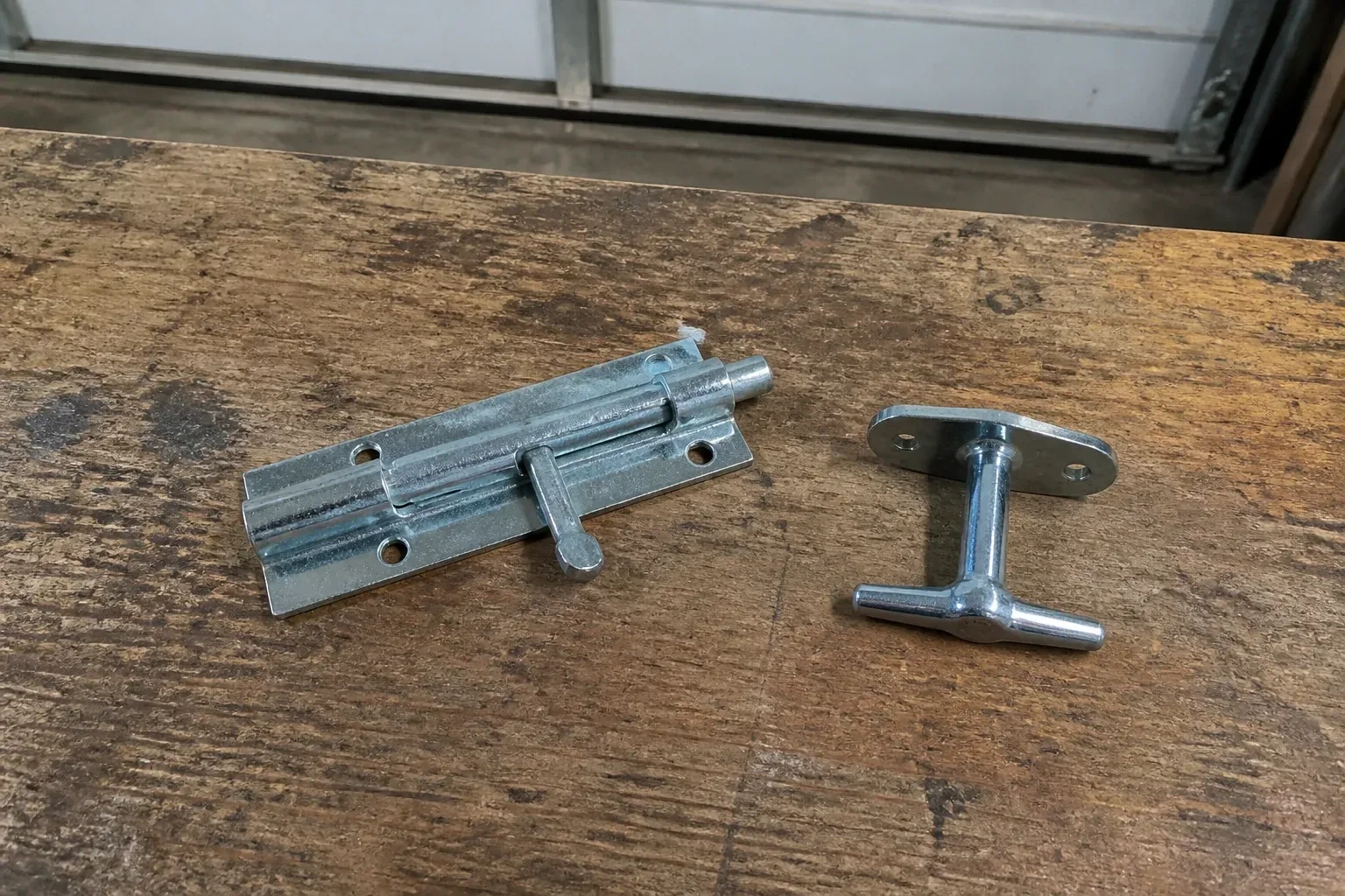 Detached slide bolt and T-handle on a wooden garage workbench. — Garage Door Manual Lock Repair, Uxbridge